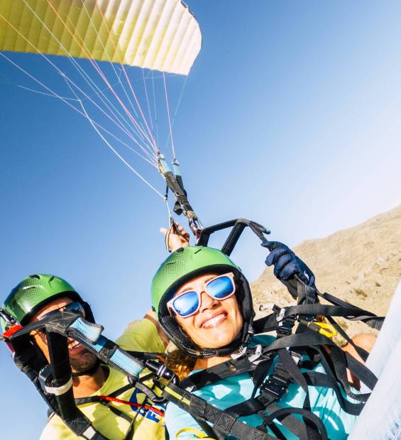 Active young adult people woman enjoy paraglide activity fliying in the sky with professional pilote in the back - cheerful happy female people fly and have fun with paragliding